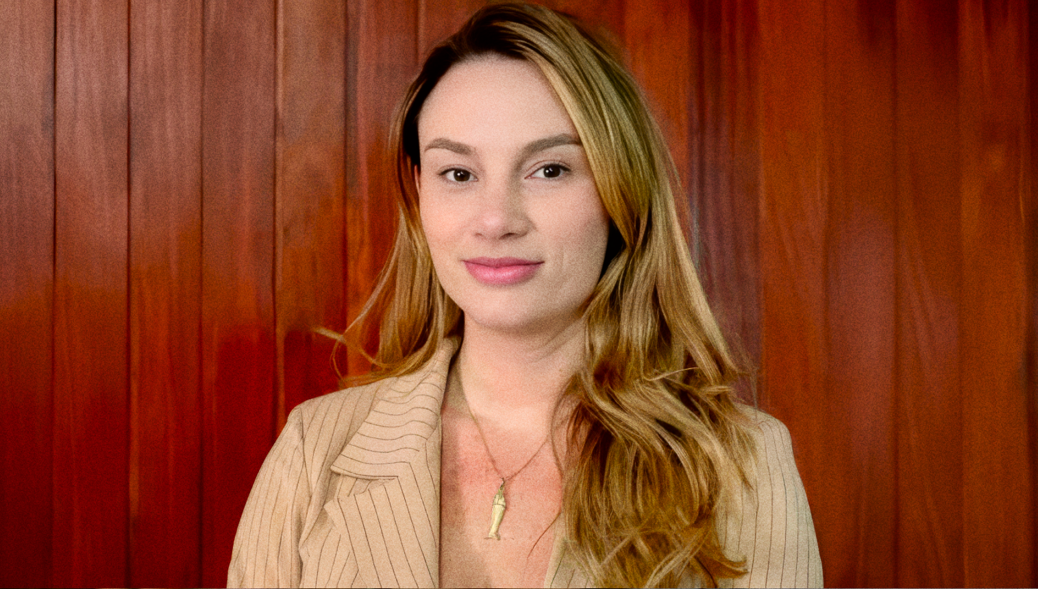 Antônia Burke, de blazer bege, diante de um painel de madeira.