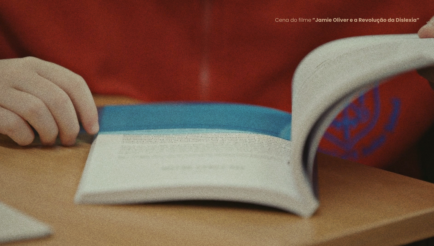 Livro aberto sobre uma mesa, com a mão de uma pessoa junto à página.